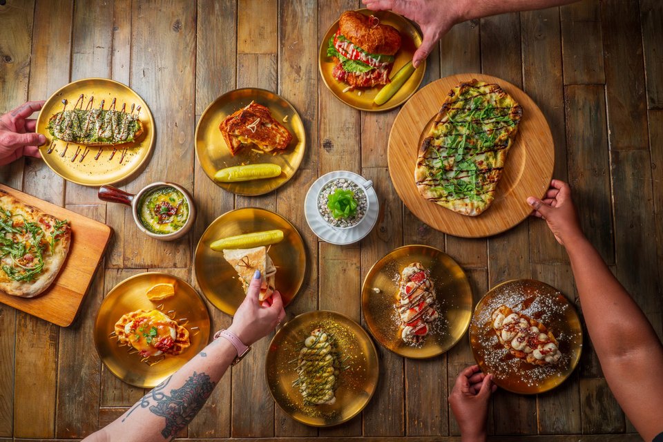 Gold plates of croffles, flatbread and paninis on a wood table at Corner Gate Coffee House